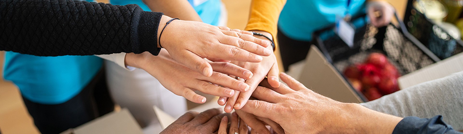 Mehrere Hände liegen übereinander als Zeichen für Zusammenhalt und Teamarbeit.